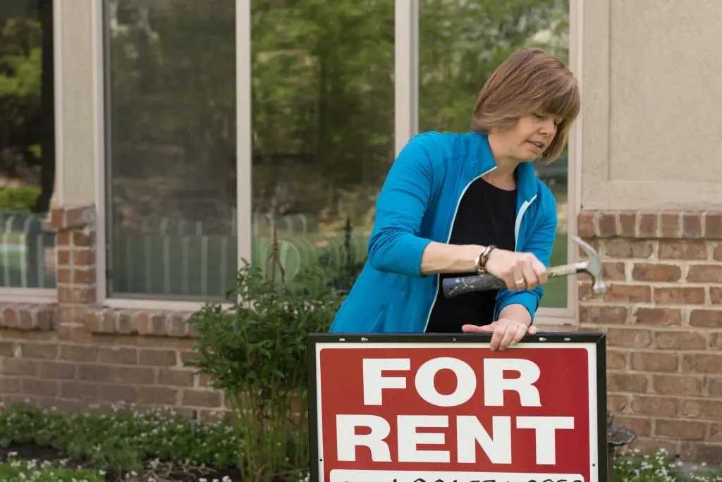 Woman placing a "For Rent" sign in yard