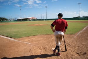 A man standing at home plate on a baseball diamond leaning on a bat