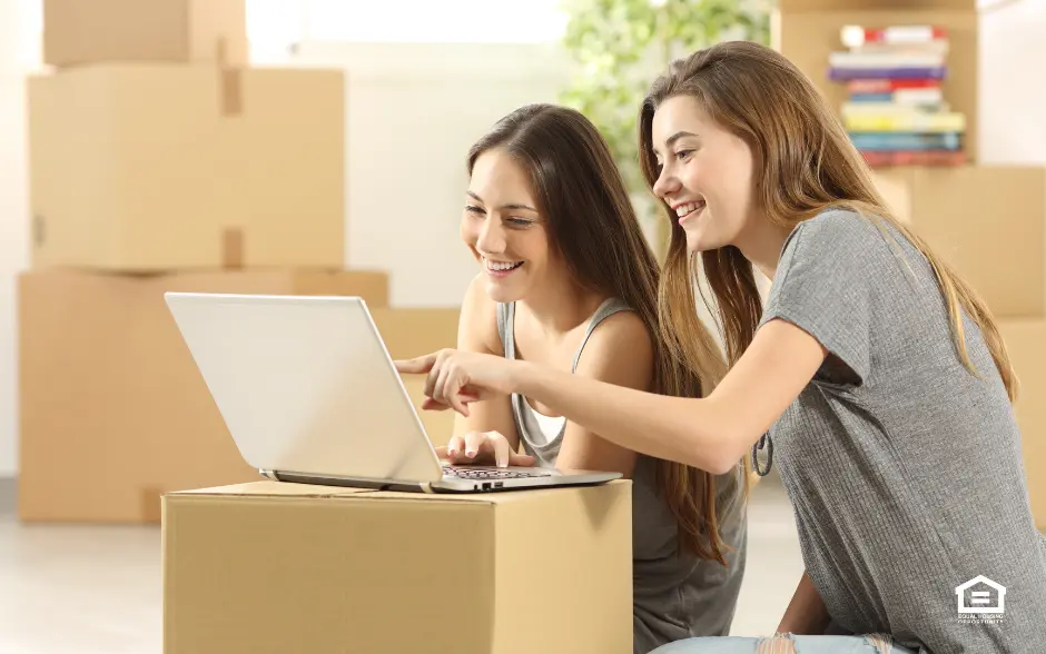 Two young women sitting on floor looking at laptop computer