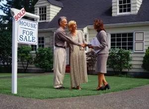 Couple with real estate agent in front of Sold sign