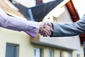 Two people shaking hands in front of a house