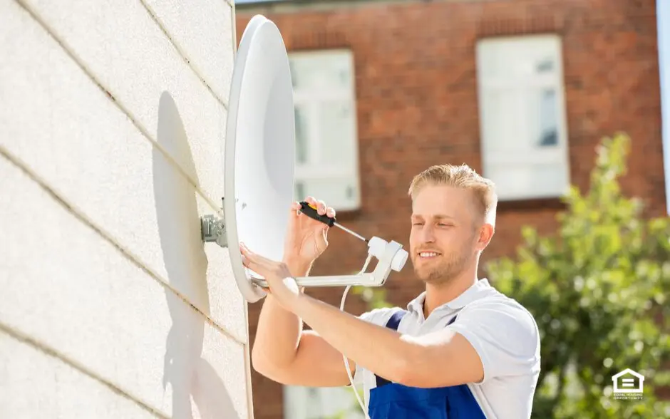Man installing small satellite dish on side of house