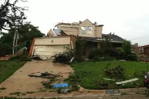 Exterior view of home destroyed by tornado with debris scattered on front lawn.
