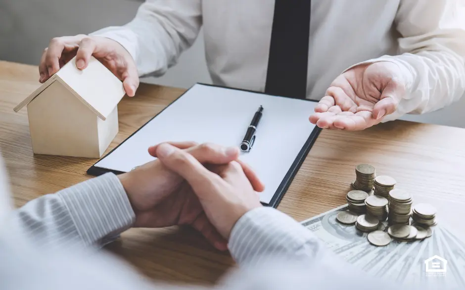 Two men talking with a notepad, wooden house and money on desk